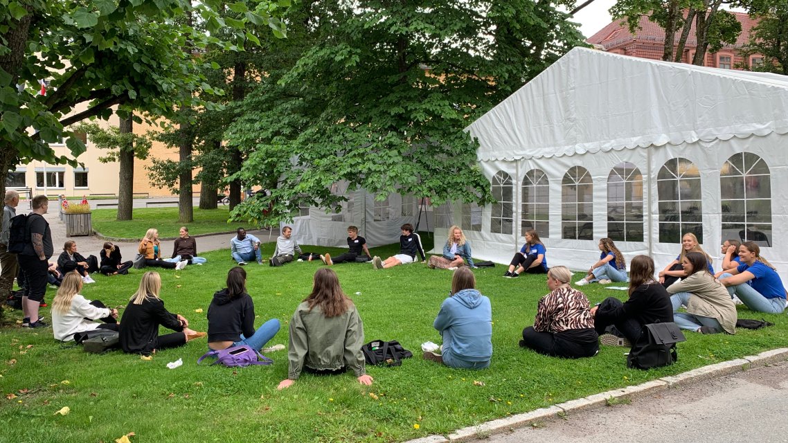 Studenter sitter i ring på en gressplen i fadderuken