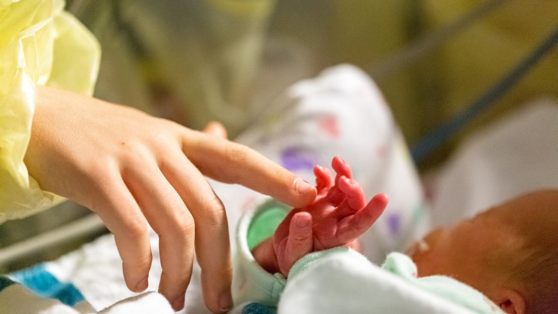 Helsepersonell holder hånden borti hånden til prematurt barn
