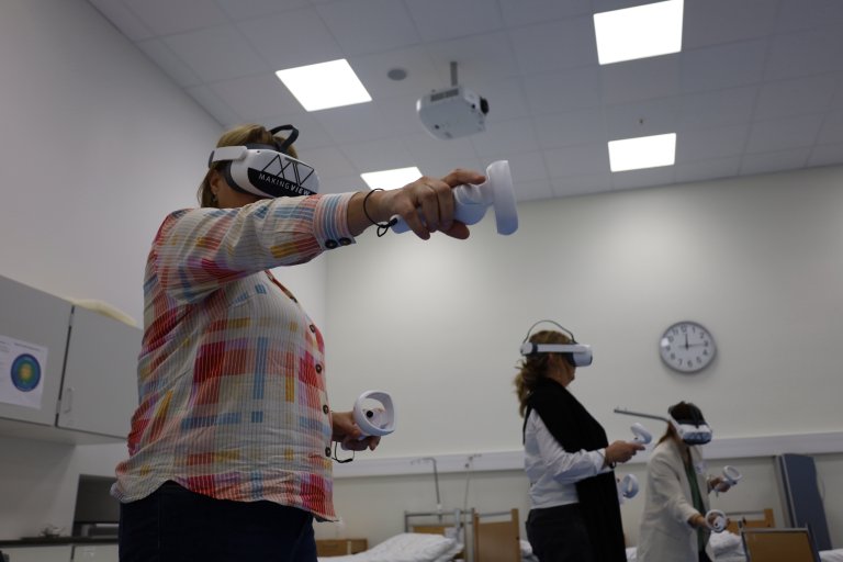 Tre damer med VR-briller, en strekker armen ut